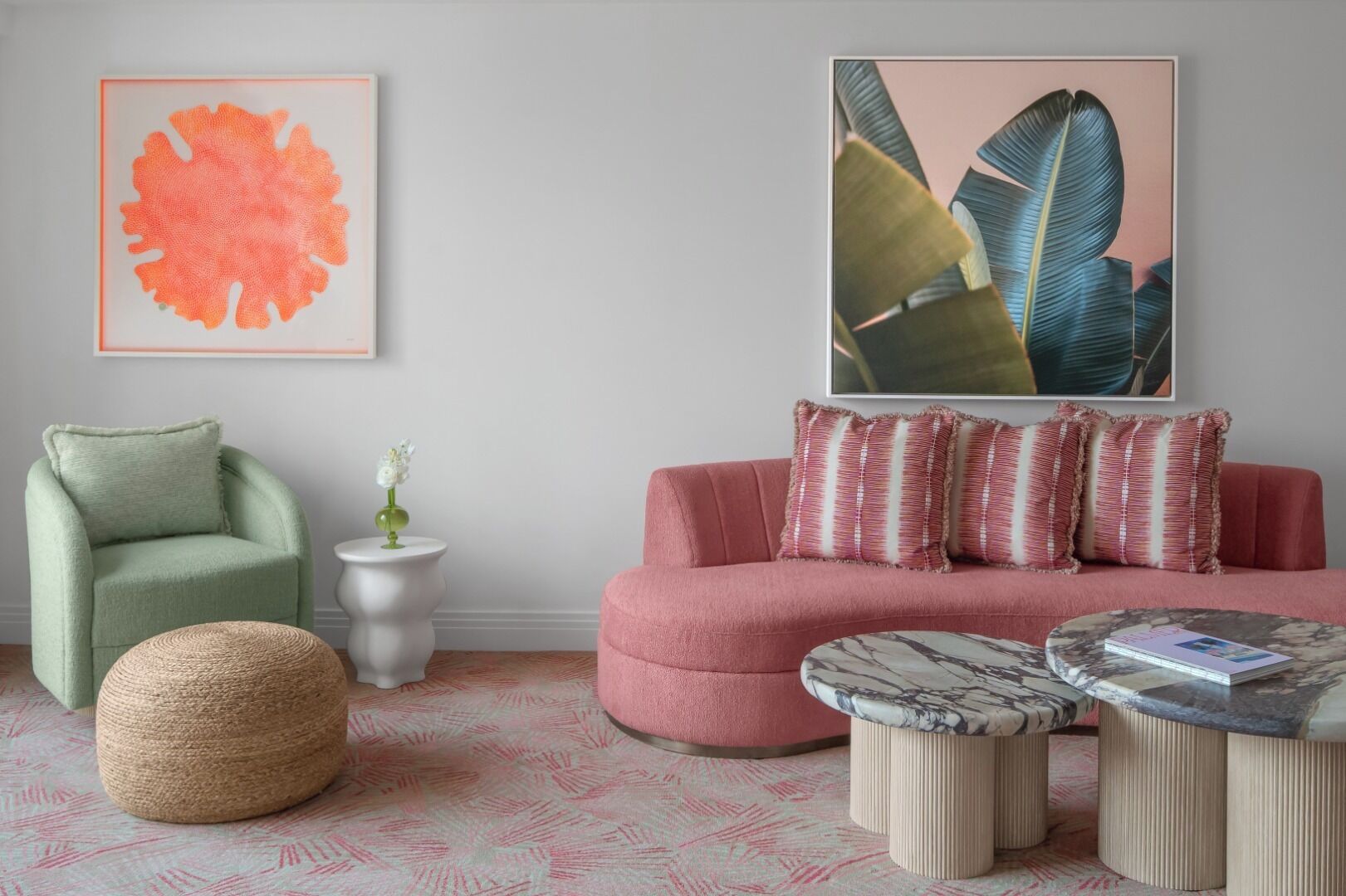 A living room with a green armchair, a pink sofa, a round ottoman, a small white side table with a vase, and a marble coffee table.