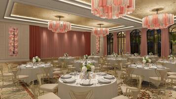 Un salón de banquetes con mesas redondas, sillas doradas y candelabros rosados.