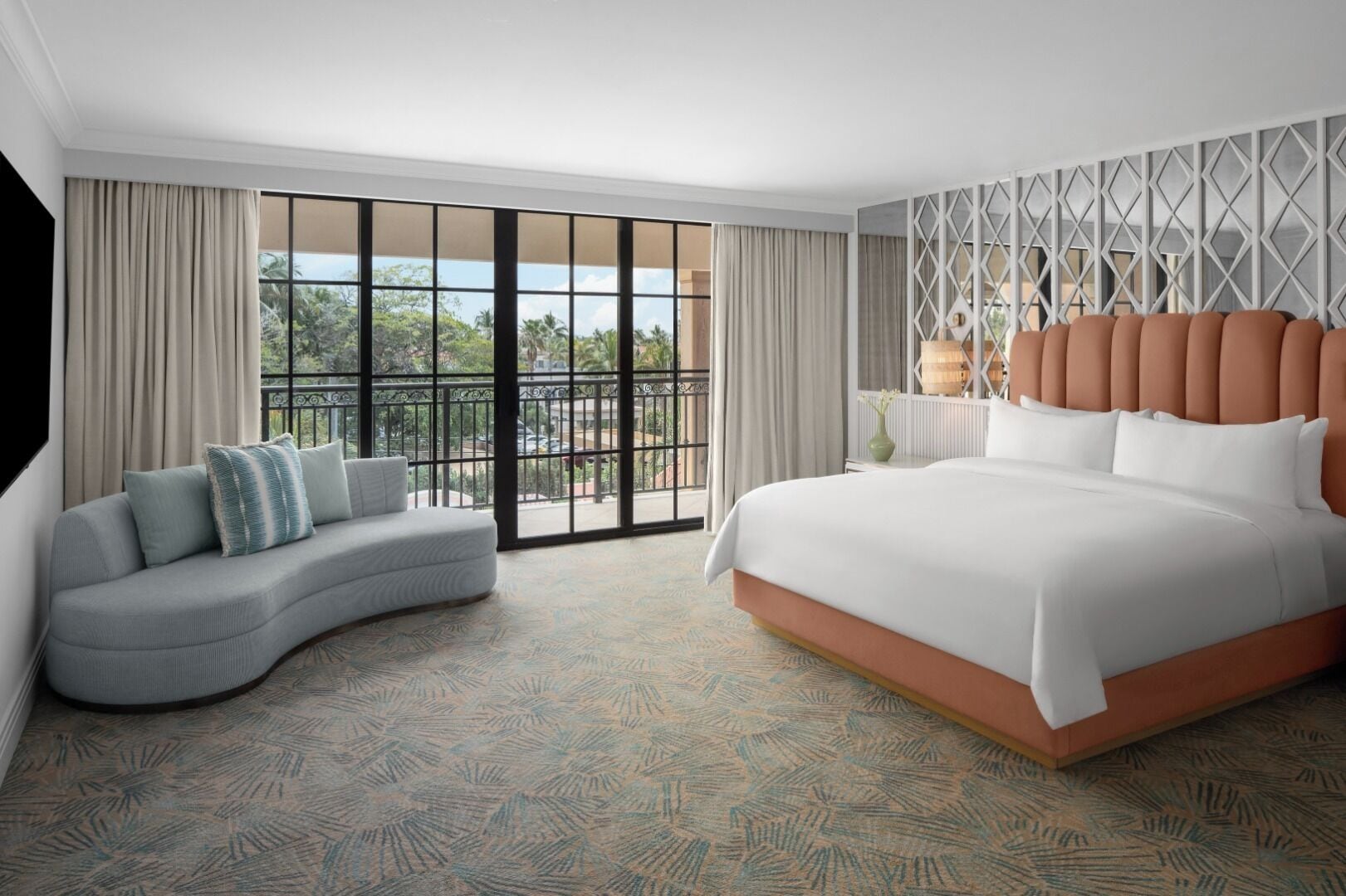 A hotel room with a large bed, a curved sofa, and a balcony with a view.