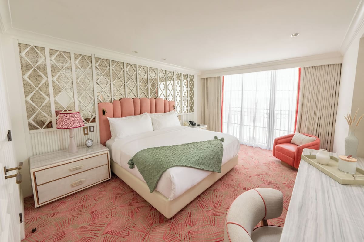 A modern hotel room with a large bed, a desk, a chair, and a window with curtains.
