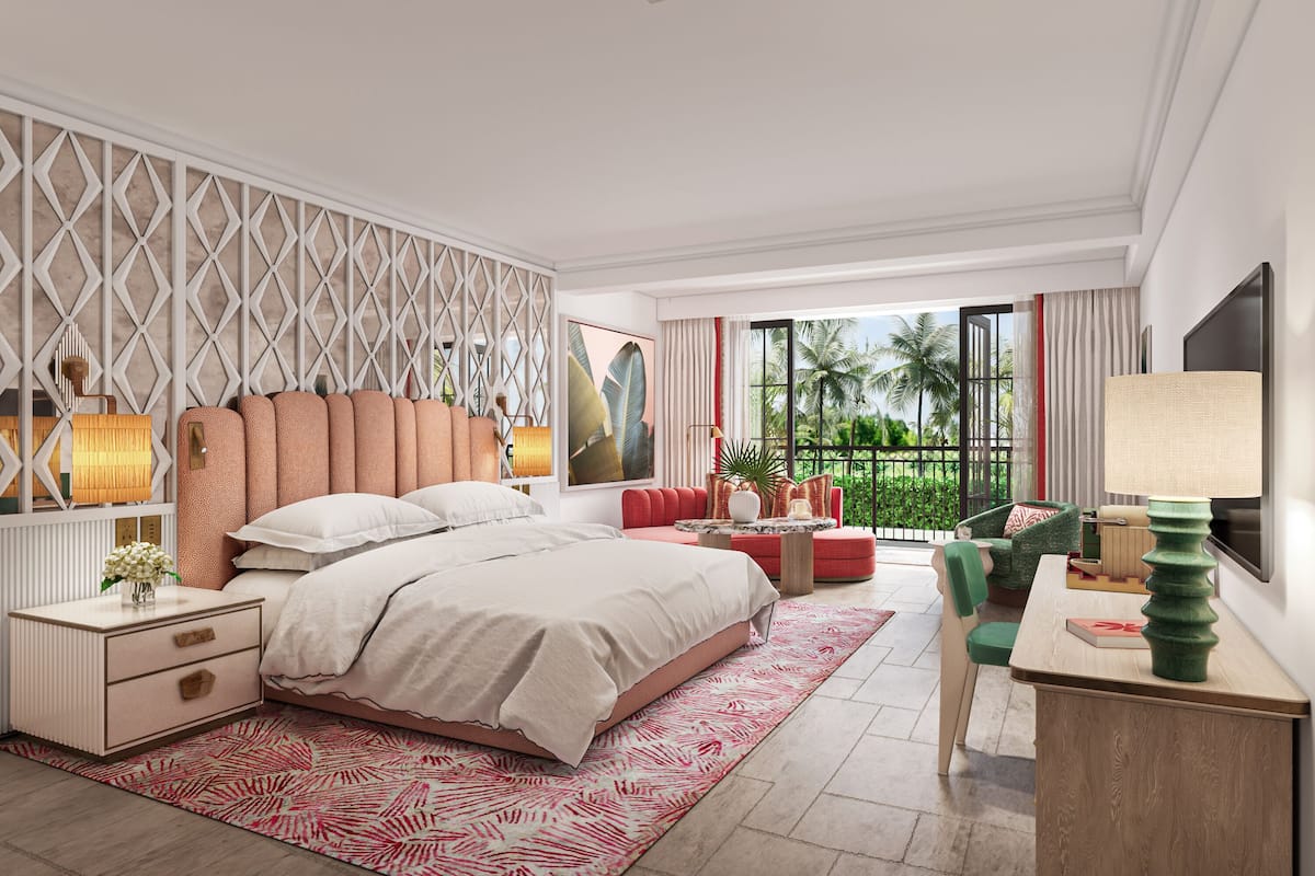 A modern bedroom with a large bed, a red sofa, a desk, and a view of palm trees through the window.