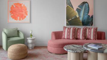 Una sala de estar con un sillón verde, un sofá rosa, un otoman redonda y una mesita de centro con un libro.
