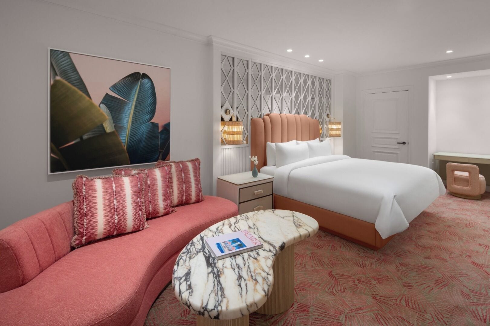Une chambre d’hôtel comprenant un lit, un canapé, une table de chevet, une table d’appoint en marbre et un luminaire fixé au mur.