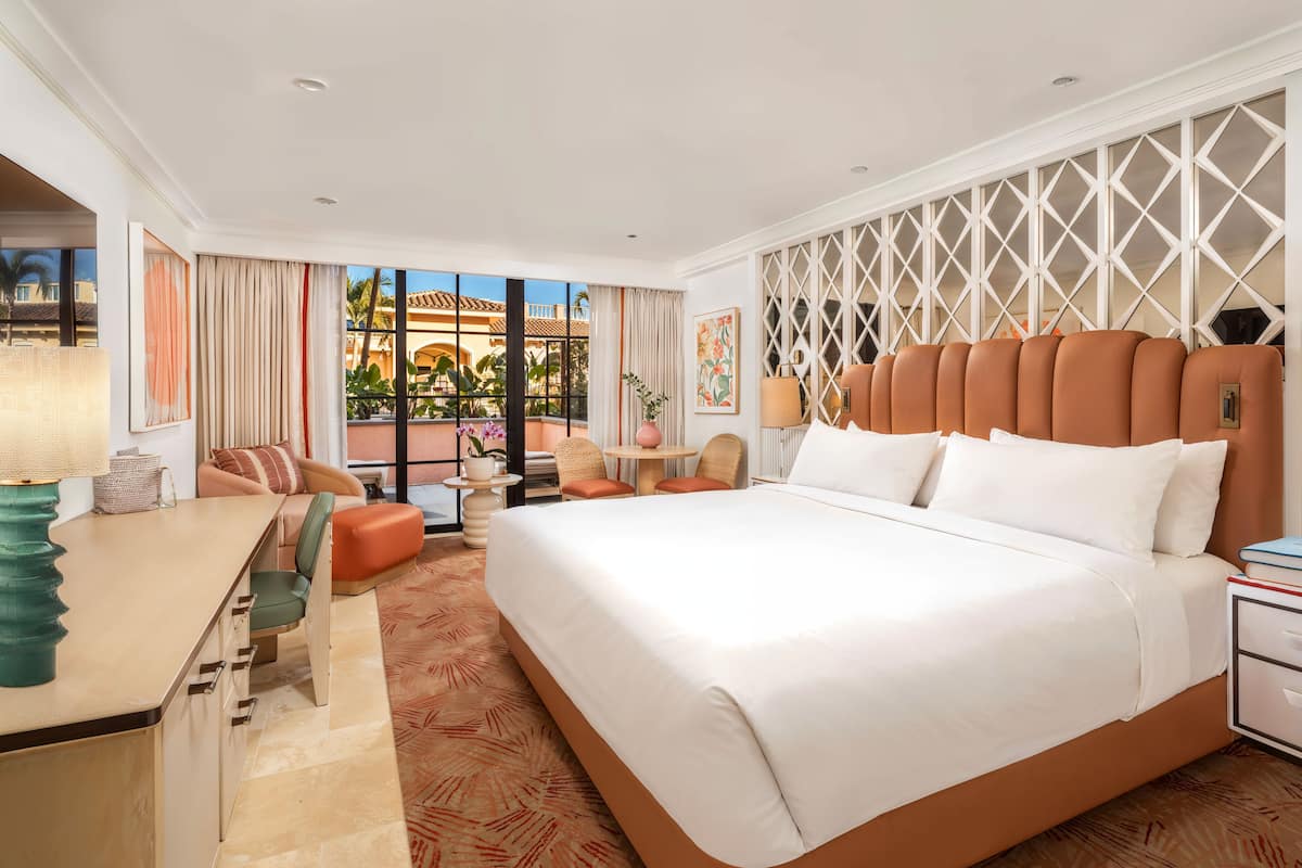 A hotel room with a large bed, a desk, and a seating area with a view of palm trees and buildings.