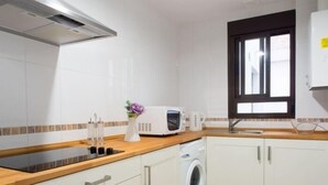 A compact kitchen with white cabinets, a built-in microwave, a washing machine, and a window with blinds. - Duque 4 · Standard Apartment without Terrace · 2 Bedrooms · 2 Bathrooms (Córdoba)