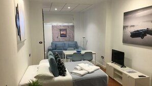 Una habitación de hotel moderna con una cama, un escritorio pequeño, un televisor y un área de comedor con sofá y sillas.