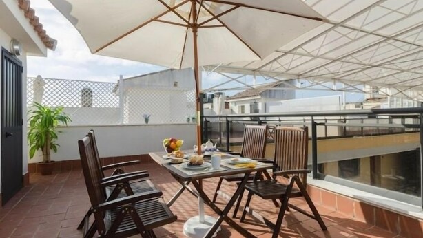 A rooftop terrace with a table set for two, a large umbrella, and a potted plant. - Duque 3 · Apartment with Terrace · 2 Bedrooms · 2 Bathrooms (Córdoba)