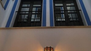 Facciata di un edificio con due finestre, ciascuna incorniciata in blu, e un piccolo fiorino da esterno sottostante.