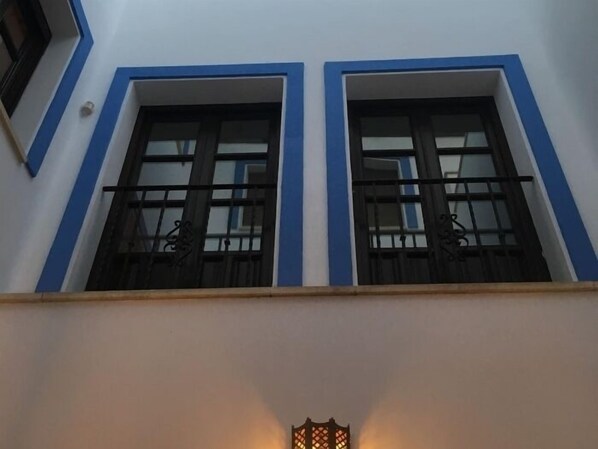 A building facade with two windows, each framed in blue, and a small outdoor light fixture below.