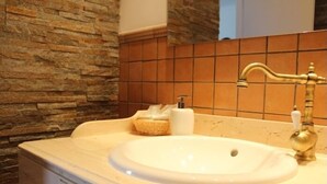 Un bagno con parete in pietra, lavandino color beige e rubinetteria dorata.