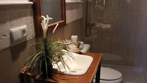 Une salle de bain avec un meuble-lavabo en bois, un lavabo blanc, une plante en pot, des toilettes et une douche séparée par une paroi de verre.