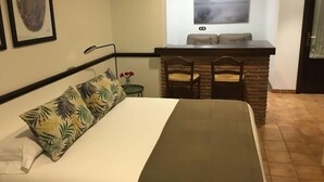 Ein Hotelzimmer mit einem Bett, einem kleinen Tisch mit Stühlen, einem an der Wand montierten Fernseher und einem Katzenbild in einem Rahmen.