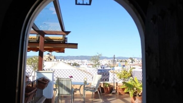 Blick von einem Balkon mit blauem Himmel, einer Holzpergola und Kübelpflanzen.