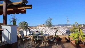 Eine Terrasse mit Tisch und Stühlen, Blumentöpfen und Blick auf Gebäude in der Ferne.