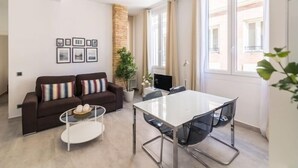 A modern living room with a sofa, coffee table, and a dining table with chairs. There are framed pictures on the wall, a potted plant, and a fireplace. - Tendillas 5 · Apartment · 2 bedrooms · 1 sofa bed · 2 bathrooms (Córdoba)