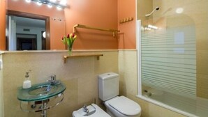 Une salle de bain avec un lavabo en verre, des toilettes et une douche dotée d’une porte en verre.