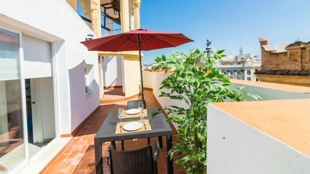 A balcony with a table set for two, a red umbrella, and a potted plant. - Tendillas · Studio with terrace · 1 bed · 1 bathroom (Córdoba)