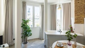 Una habitació d'hotel moderna amb un gran finestral, una zona de menjador amb taula preparada per a dues persones i una planta en test.