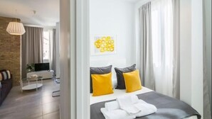 Habitació d'hotel moderna amb un llit, una televisió, una taula petita i un sofà.