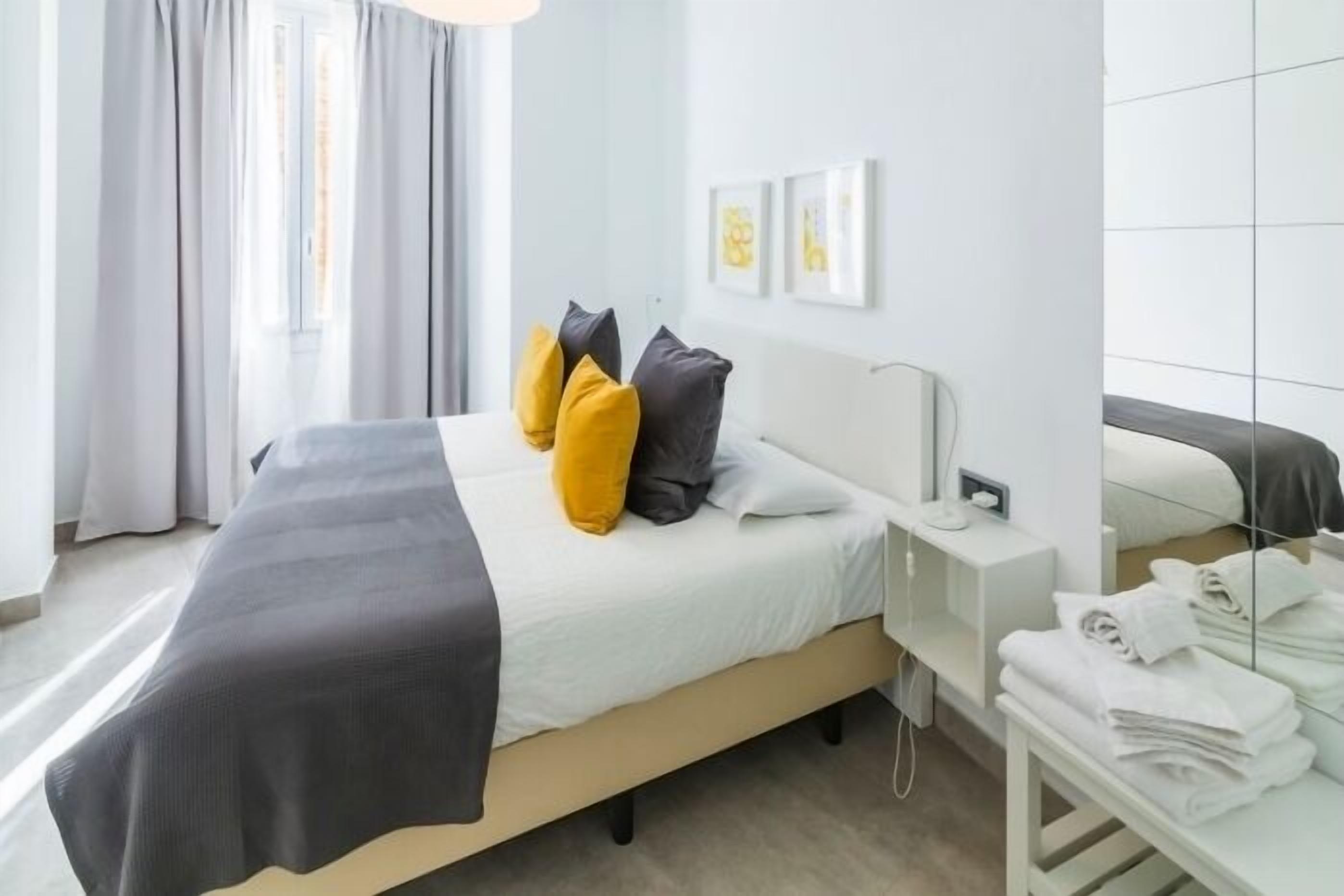 A modern hotel room with a bed, a bedside table with towels, a mirror, and artwork on the wall.