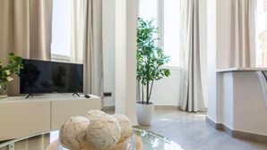 Un saló modern amb una taula de centre de vidre, un televisor de pantalla plana, una planta en test i una finestra gran amb cortines.
