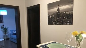 A dining area with a table set for two, a cityscape painting on the wall, and a plant with yellow flowers. - Casa del Río 4 · Standard Studio without terrace · 1 Bed · 1 Bathroom (Córdoba)