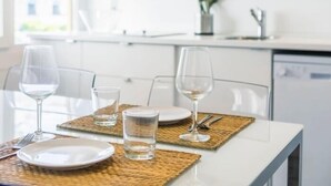 A dining table set with plates, glasses, and cutlery, with a kitchen in the background.