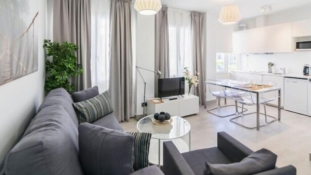 A modern living room with a grey sofa, a glass coffee table, and a dining area with a white table and chairs.