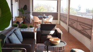 A balcony with a sofa, chairs, a table, and a bowl. There are plants and a view of the outside.