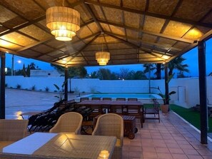 Een terras buiten met rieten meubilair en een zwembad op de achtergrond.