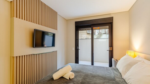 A hotel room with a bed, a television mounted on the wall, and a door leading outside. - DLH Aptos no Coração de Gramado  (Gramado)
