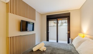 Habitación de hotel con una cama, un televisor montado en la pared y una puerta que da a un espacio exterior.