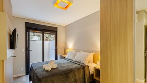 A hotel room with a bed, bedside table, lamp, and a view through a door. - DLH Aptos no Coração de Gramado (Gramado)