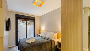 Una habitación de hotel con una cama, mesitas de noche, un televisor montado en la pared y un ventanal corredizo que da a un espacio exterior.