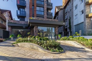 A modern building with a glass facade, outdoor seating area, and landscaped garden. - DLH Aptos no Coração de Gramado  (Gramado)