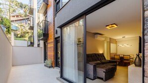 A modern apartment with a sliding glass door leading to a balcony, a dining area with a table and chairs, and a living room with a sofa and a TV. - DLH Aptos no Coração de Gramado  (Gramado)