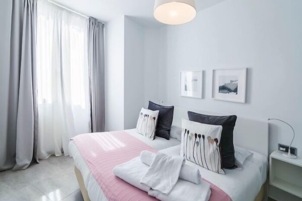 Una habitación de hotel moderna con una cama grande, una mesita de noche y una ventana con cortinas.