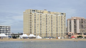 Un hôtel de grande hauteur doté de nombreux balcons, une plage en premier plan et plusieurs tentes blanches installées sur le sable.