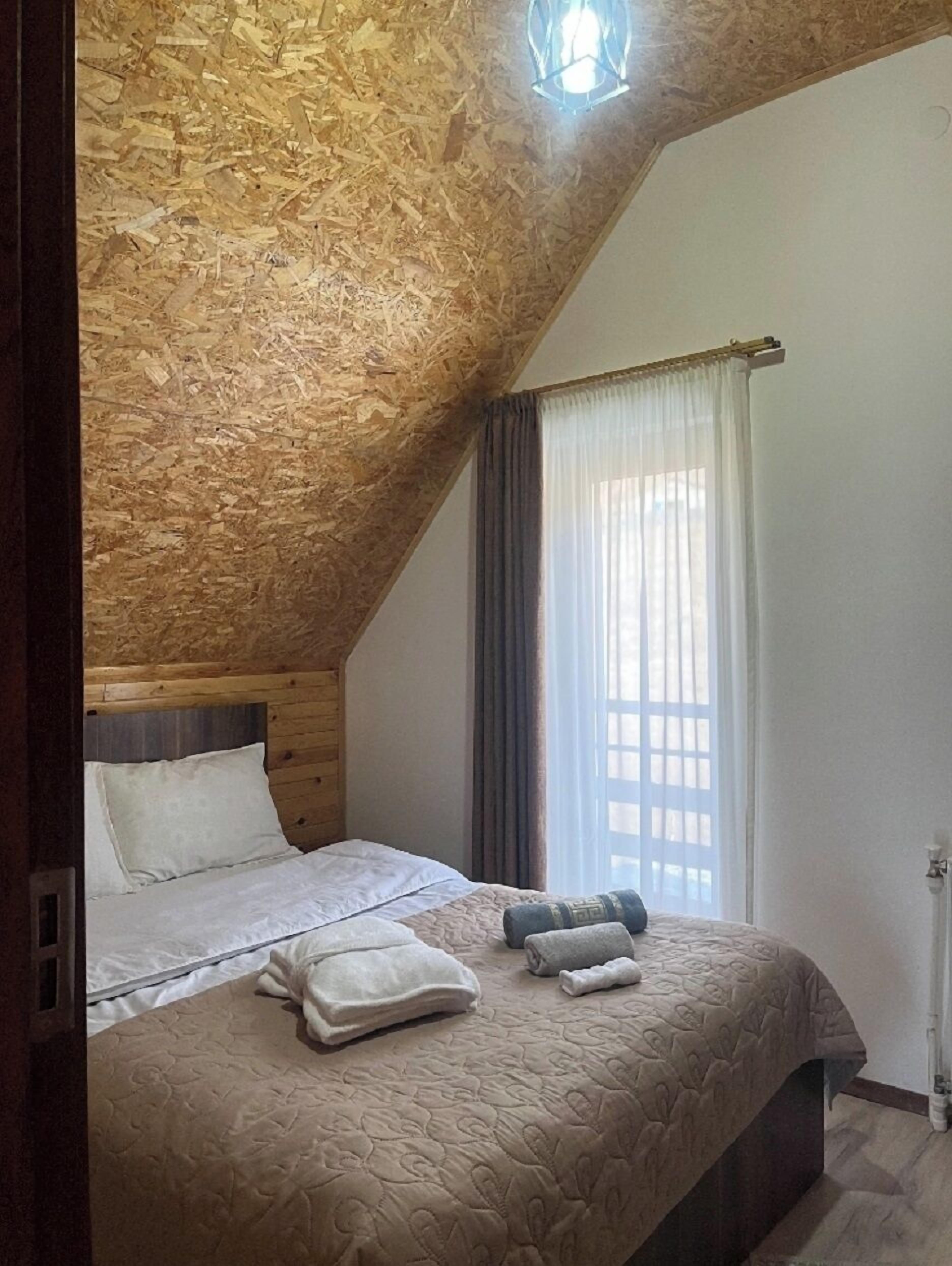A bedroom with a sloped ceiling, wooden headboard, a bed with white linens, a window with curtains, and a radiator.