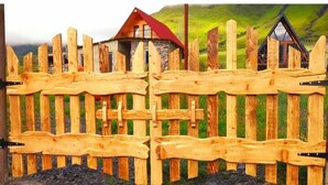 Une clôture en bois avec un portail, menant à une maison avec un toit rouge et des murs en pierre.