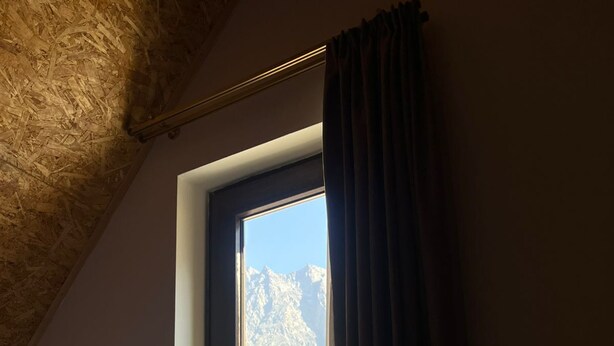 Une chambre à coucher avec un lit, une fenêtre avec des rideaux et une vue sur les montagnes.