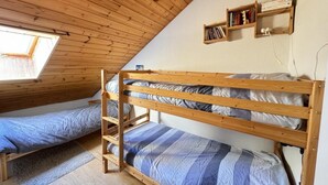 Ein Schlafsaalzimmer mit Stockbetten, Holzwänden, einem Oberlicht und einem Bücherregal.