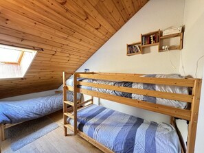 A dormitory room with bunk beds, wooden walls, a skylight, and a bookshelf.
