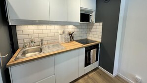 Eine kleine Küche mit weißen Schränken, einer Holz Arbeitsplatte, einer eingebauten Mikrowelle und einem Geschirrspüler.