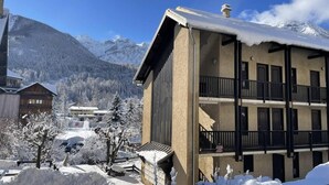 Ein mehrstöckiges Gebäude mit Balkonen, umgeben von schneebedeckten Bäumen und Bergen im Hintergrund.