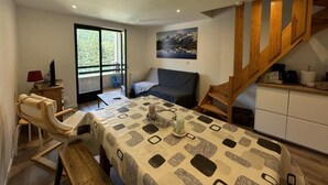 Ein gemütliches Zimmer mit Esstisch, einer Couch, einem Sessel, einer Treppe und einem Fenster.