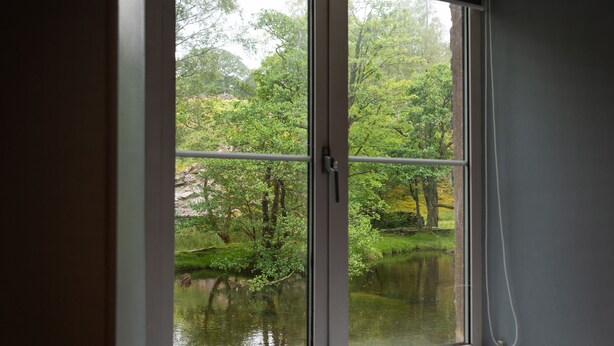 Une fenêtre donnant sur une forêt et un plan d’eau.