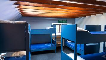 A dormitory room with bunk beds, a fire exit sign, and a window.