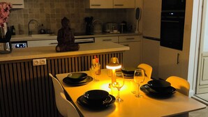 Une cuisine moderne avec des meubles blancs, une table à manger dressée avec des assiettes et des verres, et une statue de Bouddha posée sur le comptoir.