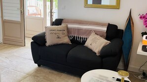 Un salon avec un canapé noir, une table ronde blanche, un miroir avec un cadre doré et une planche de surf.